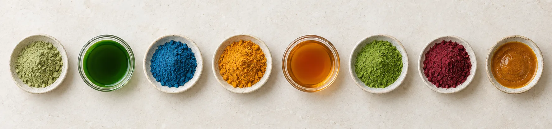 Natural ingredient powders and extracts in small dishes: green tea extract, chlorophyll, blue spirulina, turmeric, amber tea extract, matcha, beetroot and spice oleoresin